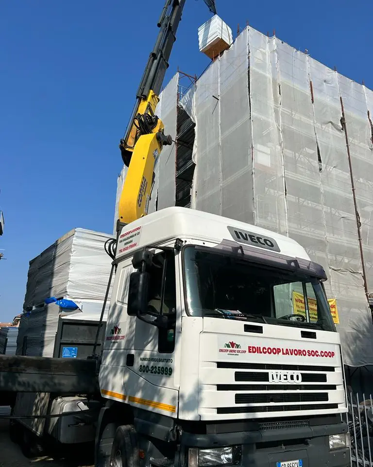 Camion Edilcoop con gru che porta il materiale su un cantiere con il ponteggio