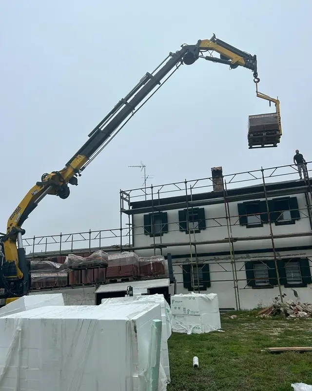 Gru Edilcoop che solleva i bancali di materiale sul tetto