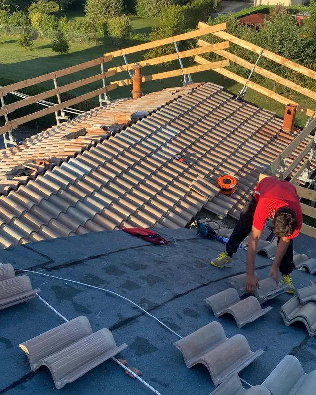 Operaio Edilcoop che posa le tegole sulla guaina, con i parapetti di sicurezza in legno sul bordo del tetto